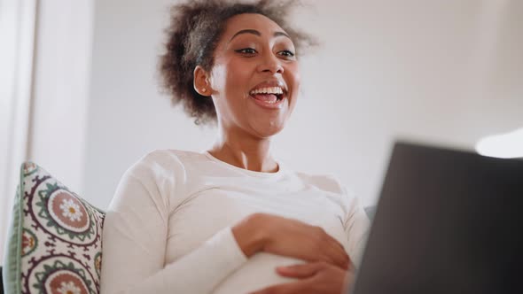 Smiling African pregnant woman talking by video call on laptop