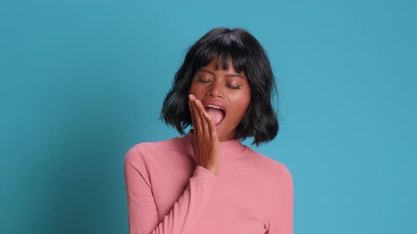 Dark Skinned Woman Yawns with Her Mouth Wide Open on a Background of Blue Wall