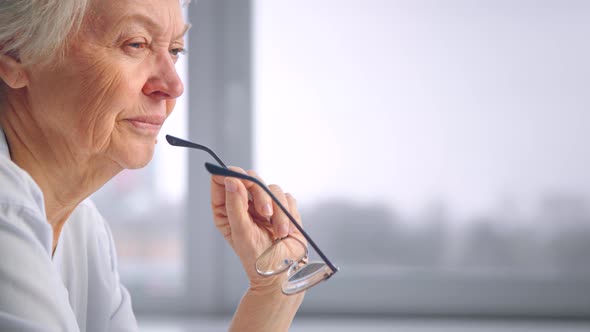 Old grandmother holds glasses in wrinkly hand with serious face