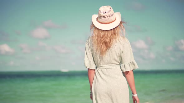 Woman Relaxing On Bahamas Flowing Dress Blowing In Wind. Woman In Hat Walks Along Beach On Caribbean