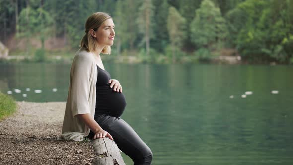 Pregnant Woman Touching Gently Her Tummy When Sitting Near the Mountain Lake.