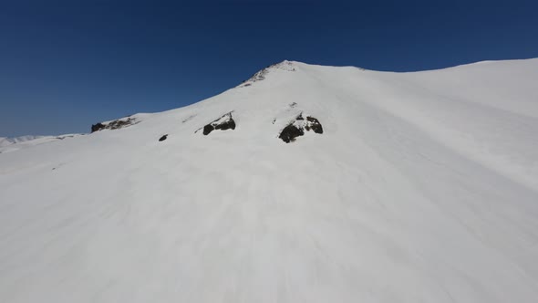 Climbing Near Soft Smooth Snow Cover Surface on High Mountain Peak Under Blue Sky Aerial View