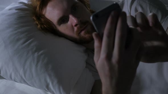 Redhead Beard Man on Smartphone Browsing Email and Messages in Bed