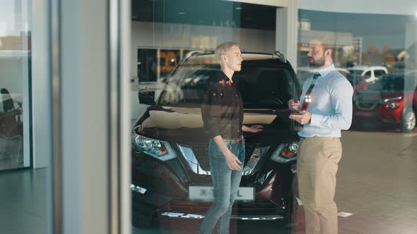 Adult Female Customer and Smiling Male Car Dealer Standing at Car Salon Interior