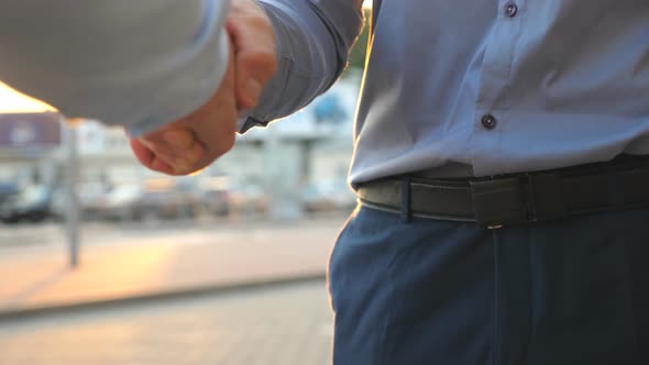 Dolly Shot of Two Young Colleagues Meeting and Shaking Hands at City Street on Sunset