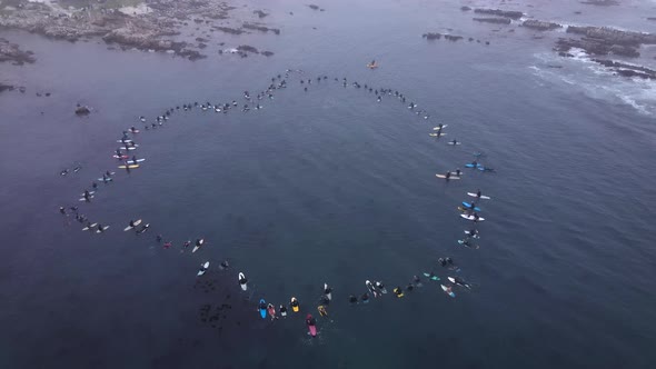 Solidarity at paddle-out in ocean for passing of a surfer; tribute to person's life, ascending aeria