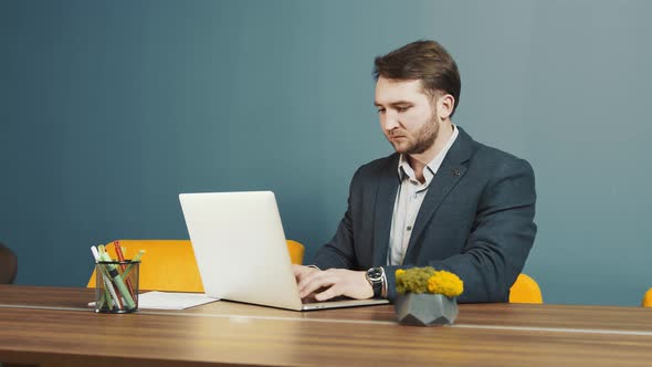 Young Bearded Man Programmer Caucasian Appearance Sitting and Working on a Laptop