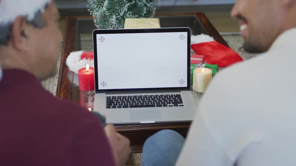 Happy son and father making christmas video call on laptop with blank white screen and copy space