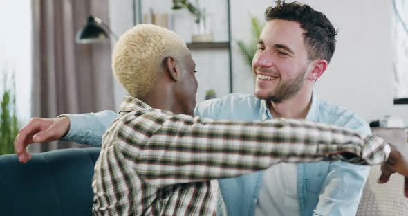 Young Mixed Race Gays Tenderly Embracing Each Other Sitting on the Couch at Home