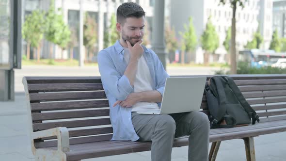 Thinking Young Man Using Laptop While Sitting on Bench