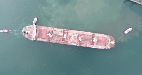 Large cargo ship enters the port escorted by tugboats.