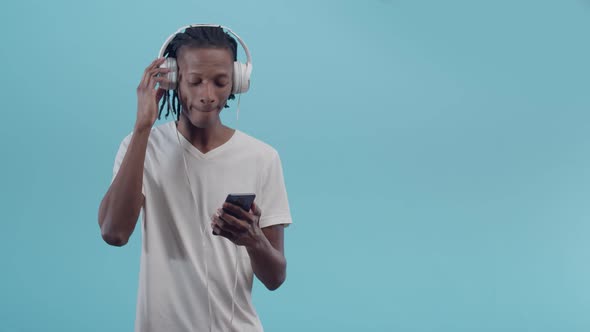 Black man with headphones listens to music and uses phone dancing in the studio.