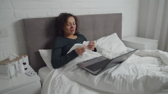 Sick Adult Woman Lying in Bed Watching Video Movie on Laptop Indoors