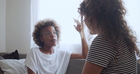 Two Multiethnic Female Friends Talking to Each Other on the Sofa in a House