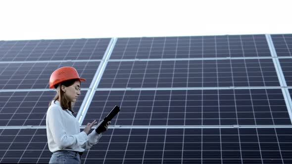 Beautiful young engineer standing near solar panels outdoors, Green Energy Concept.