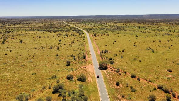 Long drone shot of a car driving into the distance of a never ending road in the country