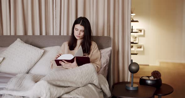 Woman Relaxing in Bed and Reading a Book in the Bedroom in the Modern House