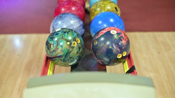 Camera zooms in on the bowling ball rack, hand picking up one of the balls