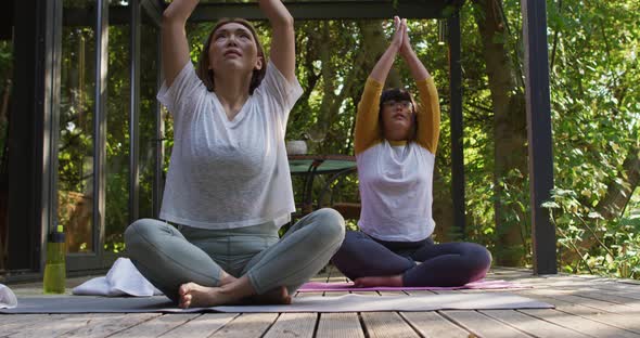 Asian mother and daughter practicing yoga outdoors in garden