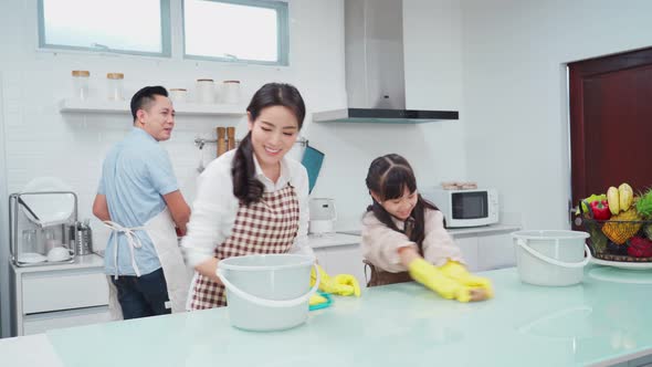 Asian young family parents teaching their little kid daughter to clean kitchen counter in house.