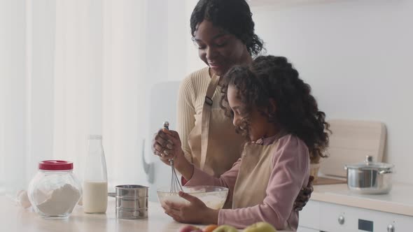 Happy African American Mother Teaching Her Daughter to Cook Dough Mixing Ingredients in Bowl