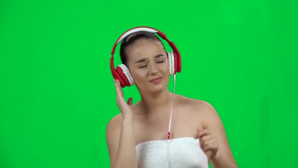 Cheerful Girl in White Towel Enjoying Music in Big Red Headphones. Green Screen. Slow Motion