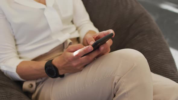 Midsection of caucasian businesswoman sitting in armchair and using smartphone