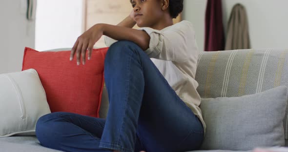 Thoughtful african american woman sitting on sofa in living room