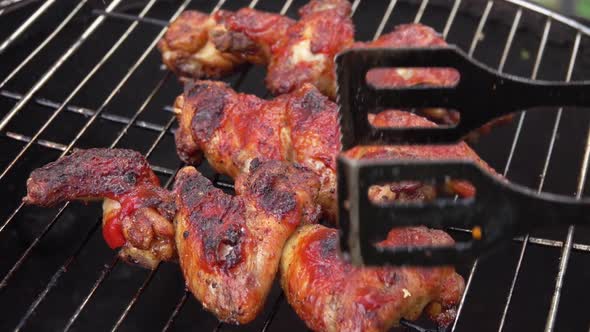 Closeup of the Chicken Wings Rotated on the Grill Grid with Metal Tongs