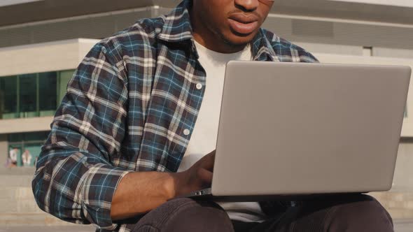 Moving Footage African American Guy Student in Sunglasses Sitting on Street in City Uses Laptop