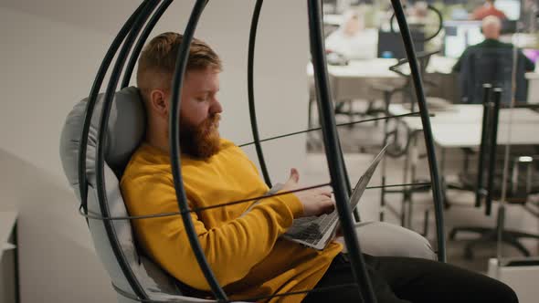Male Using Laptop Working Sitting In Swing Chair In Office