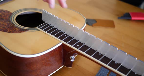 Close up on the hands of a luthier craftsman leveling an acoustic guitar neck and fretboard while ad