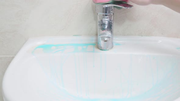 A Hand with a Pink Sponge Without Rubber Gloves Thoroughly Washes the White Sink and Faucet in the