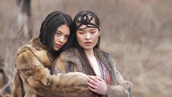 two Asian young women in ethnic clothes are embracing and posing in the steppe in nature. Slow mo