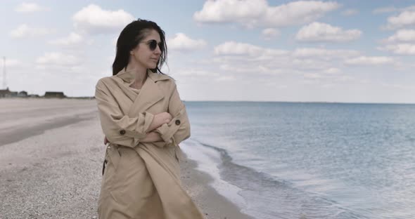 Portrait of Girl in sunglasses and cloak walks on an empty sandy beach. Seaside background.