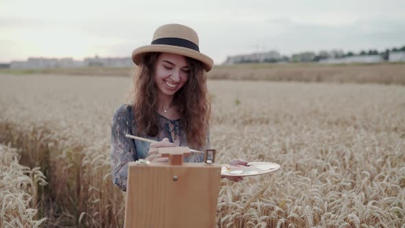Cheerful Young Lady in Hat Painting with Watercolors Among Ripe Wheat