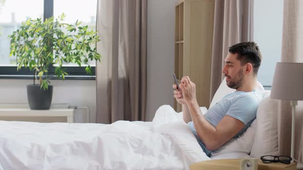 Happy Man with Smartphone in Bed at Home