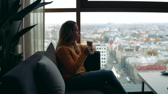 A Lady Is Drinking Coffee and Looking Into the Window with a City View