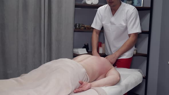 Masseur in Uniform Massaging Man's Body in Massage Room