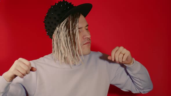 Young handsome man with dreadlocks in black cap dancing on red background.