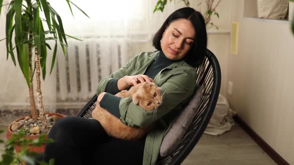 Woman Sitting on the Armchair Holding Cute Ginger Cat at Green Home