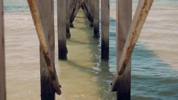 Underneath an old wooden pier looking out to sea. Beautiful clear ocean waters lap at the structures