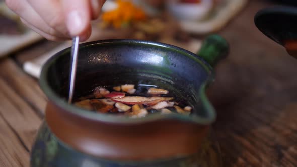 Close Up of Stirring Hot Tea in a Traditional Tea Pot. Flowers and Pieces of Dry Fruit on Teaspoon. 