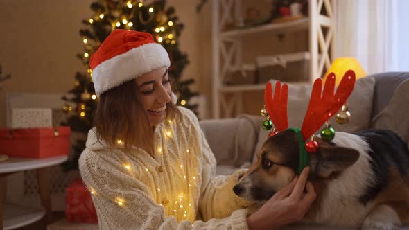 Broll of Smiling Tender and Affectionate Woman in Santa Hat Putts on Reindeer Antlers Headband on