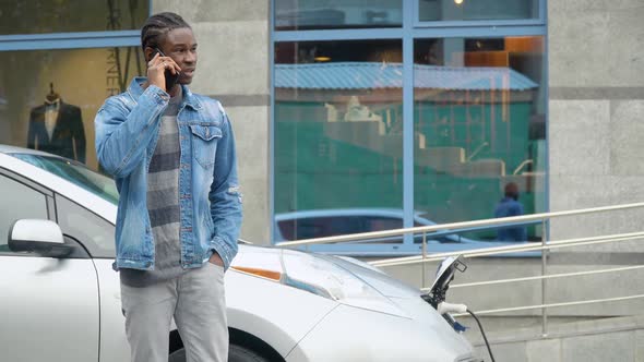 African American Man Talking Phone While Charging Electric Car