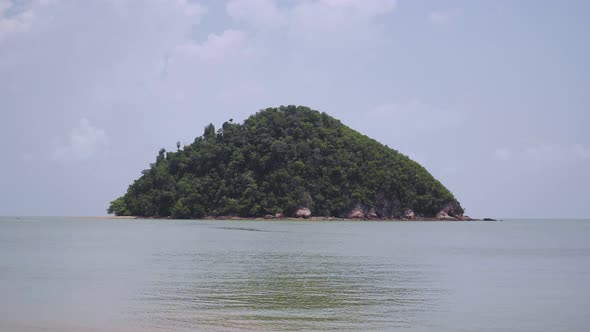 Small tropical mountain island with tree, rock in the middle of sea and cloudy blue sky. Landscape