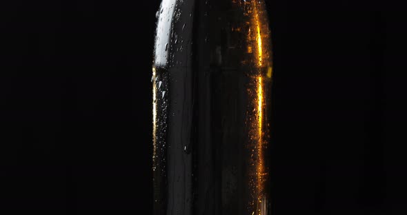 Bottle of Cold Beer on a Black Background. It Slowly Rotates. Condensate