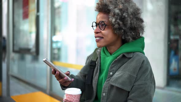 Happy adult African woman wearing casual clothes looking around and typing by phone