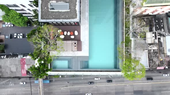 Top View Of An Infinity Pool At The Hotel Rooftop With Man Sitting On The Lounge Using Laptop