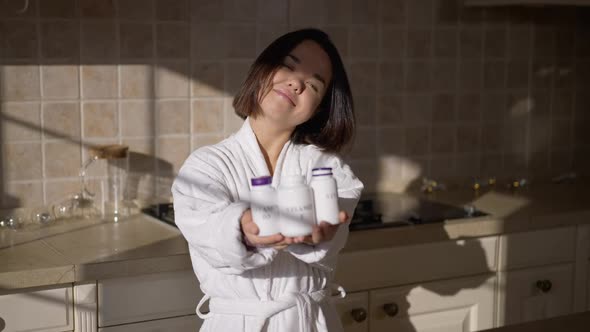 Smiling Adult Little Woman Posing with Vitamin Bottles in Kitchen at Home on Sunny Morning